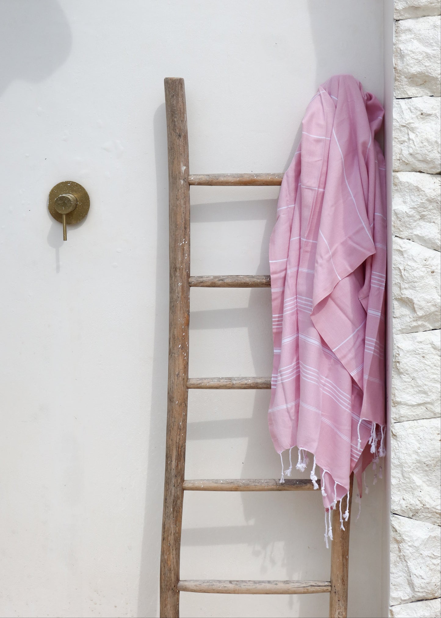 Pink towel draped over a wooden ladder against a white wall.