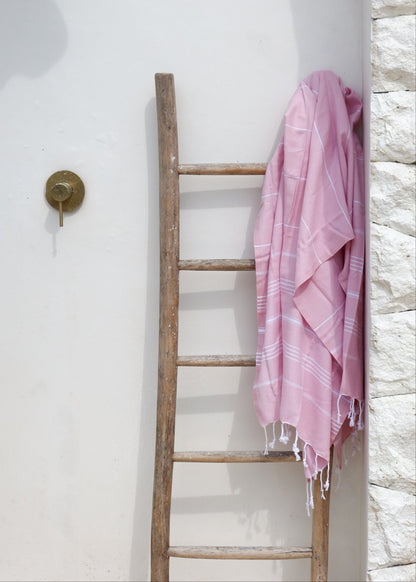 Pink towel draped over a wooden ladder against a white wall.