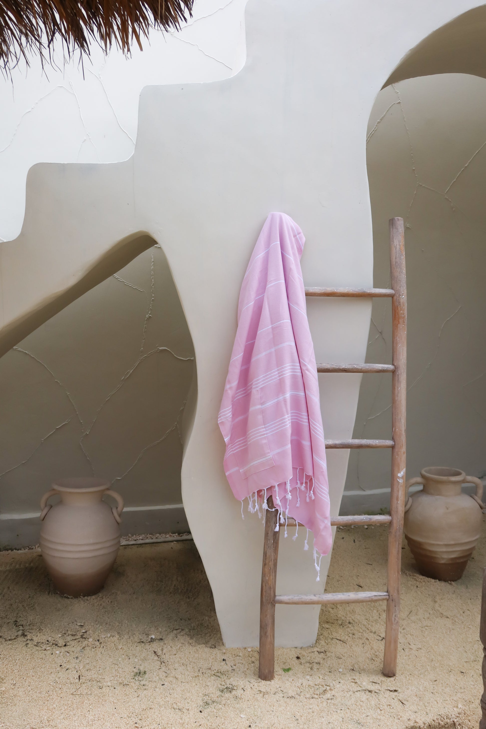 Pink towel draped over a wooden ladder against a white wall with decorative vases.
