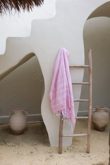 Pink towel draped over a wooden ladder against a white wall with decorative vases.